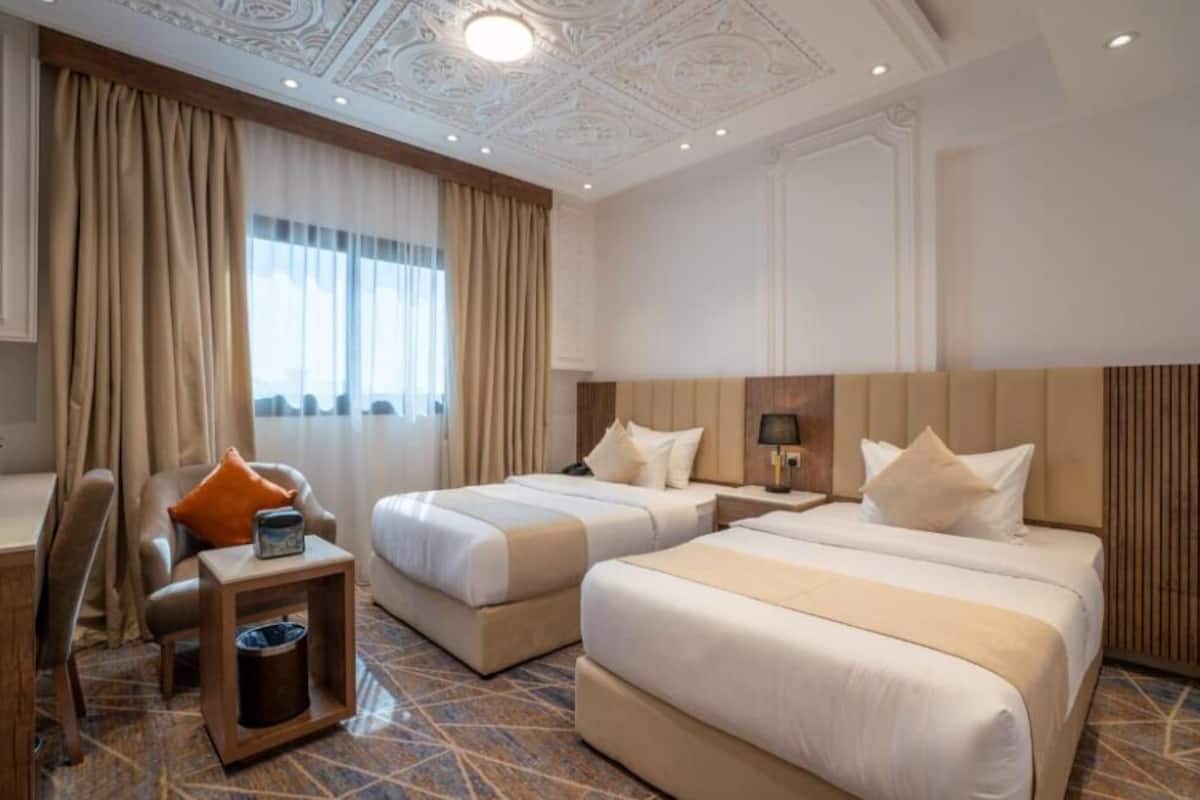 A hotel room with two beds, a desk, a chair, and a window with curtains.