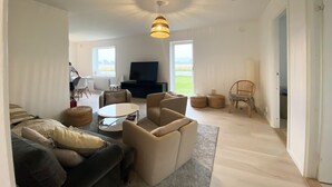 Een ruime woonkamer met een grote televisie, comfortabele zithoek en uitzicht op het groen.