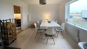 Een eethoek met een witte tafel, witte stoelen, een vloerlamp en uitzicht op een vrachtwagen buiten.