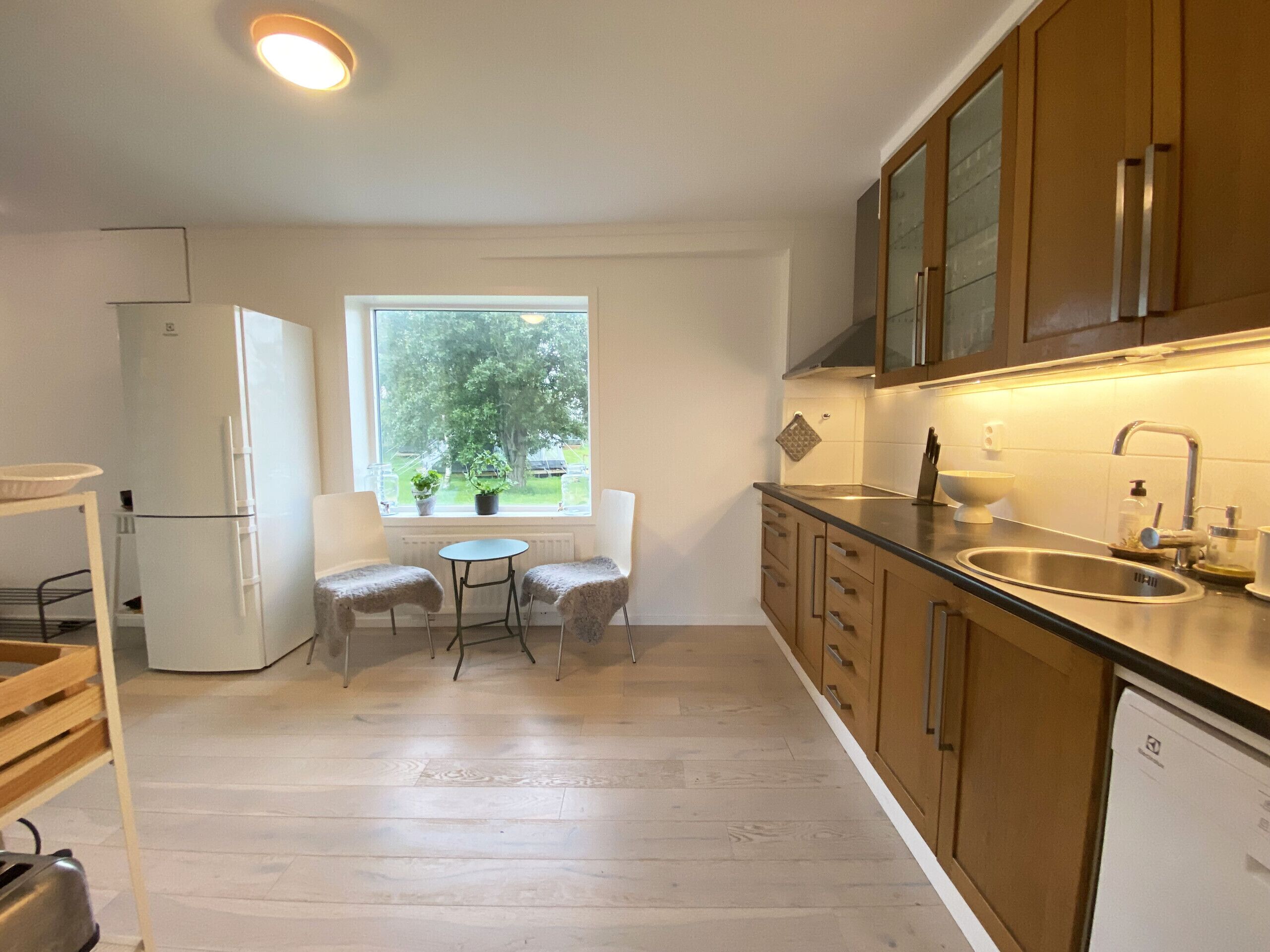 Une cuisine moderne avec une fenêtre, deux chaises, un réfrigérateur et des armoires en bois.