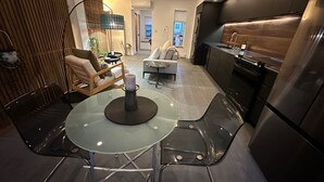 Een moderne keuken met een roestvrijstalen koelkast, een eethoek met een glazen tafel en stoelen, en een zithoek met een bank en een lamp.