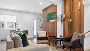 Een moderne woonkamer met een bank, twee fauteuils, een houten accentmuur en een hanglamp.