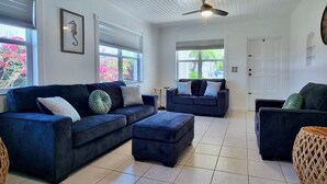 A living room with two dark blue sofas, a small ottoman, a wicker side table, and a ceiling fan.