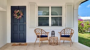 A front door with a wreath, two wicker chairs with blue cushions, a small table, and a doormat.