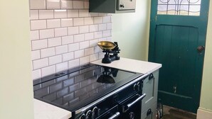 Una cocina con estufa negra, azulejos blancos y puerta verde.