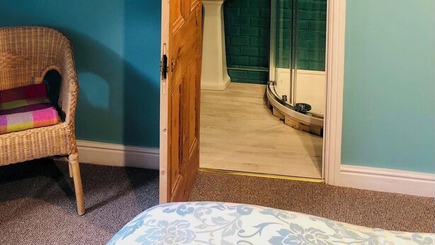 Una habitación con techo inclinado, una silla de mimbre, un lavamanos pequeño y una cabina de ducha de vidrio.