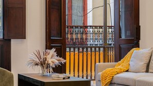 A living room with a sofa, a coffee table with a vase and books, and a view of a balcony with a railing. - Soho House The Grand Patio (San Juan)