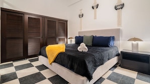 A bedroom with a checkered floor, a bed with a black and grey bedspread, a yellow throw blanket, and three wall-mounted macramé hangings. - Soho House The Grand Patio (San Juan)