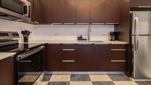 A modern kitchen with dark wooden cabinets, stainless steel appliances, and a checkered tile floor. - Soho House The Grand Patio (San Juan)