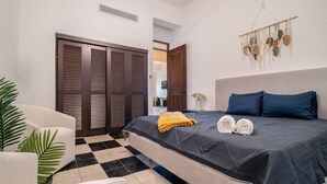 A hotel room with a bed, a chair, a potted plant, a wall-mounted decor, and a checkered floor. - Soho House – Inspired by RH (San Juan)