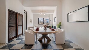 A modern dining area with a round table, white chairs, and a central light fixture. - Soho House – Inspired by RH (San Juan)