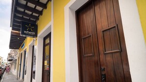 A street view with a yellow building featuring a wooden door and a sign for 'whetu tattoo shop'. - Soho House – Inspired by RH (San Juan)