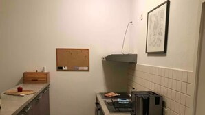 A compact kitchen with a built-in stove, a coffee maker, and a corkboard on the wall. - Modern apartment, Randneustadt with excellent connections (Dresden)