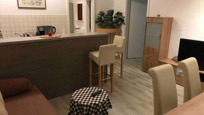 A compact living space with a kitchenette, a dining area with a small table and chairs, a sofa, and a TV. - Modern apartment, Randneustadt with excellent connections (Dresden)
