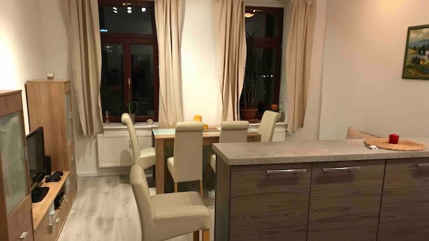 A modern kitchen with a dining area, featuring a wooden cabinet, a TV, and a dining table with chairs. - Modern apartment, Randneustadt with excellent connections (Dresden)