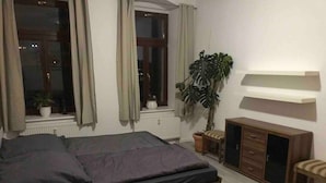 A bedroom with a large bed, a wooden cabinet, a potted plant, and a window with curtains. - Modern apartment, Randneustadt with excellent connections (Dresden)