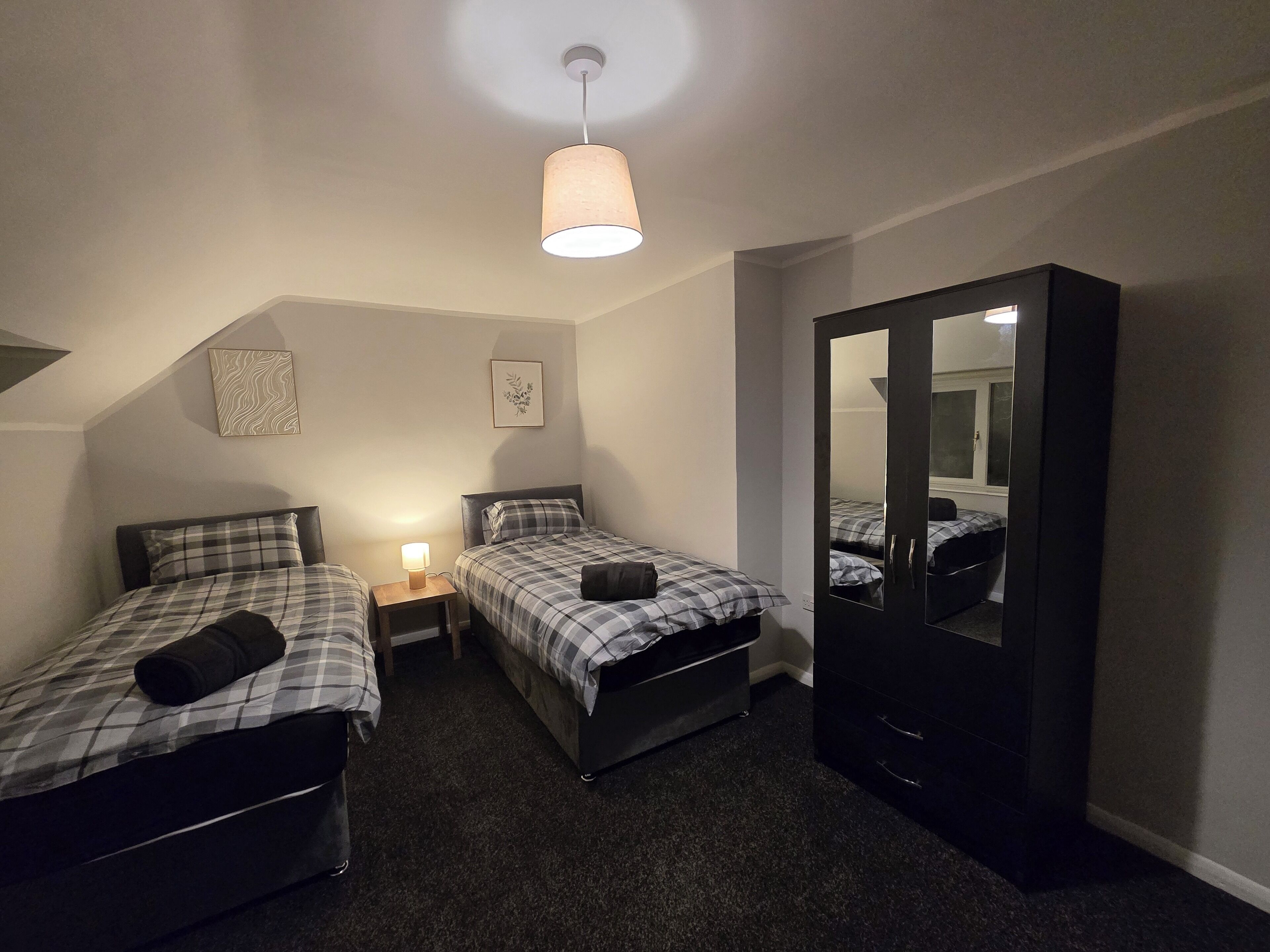 Une chambre avec deux lits, une table de chevet avec une lampe, une armoire et un luminaire au plafond.