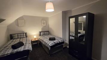 Une chambre avec deux lits, une table de chevet avec une lampe, une armoire et un luminaire au plafond.