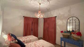 A bedroom with two beds, a chandelier, a mirror, and a small table.