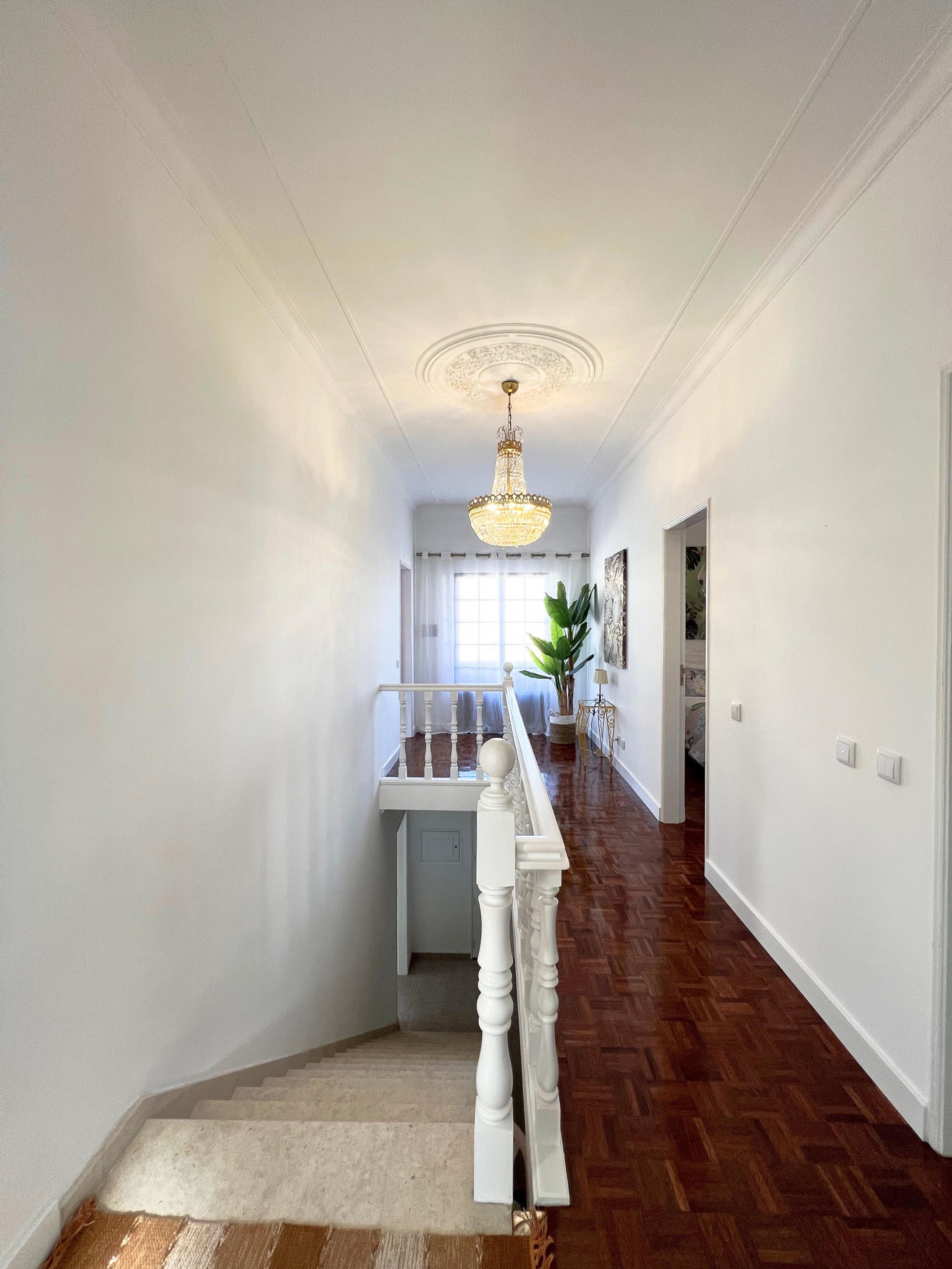 A hallway with a wooden floor, white walls, and a chandelier.
