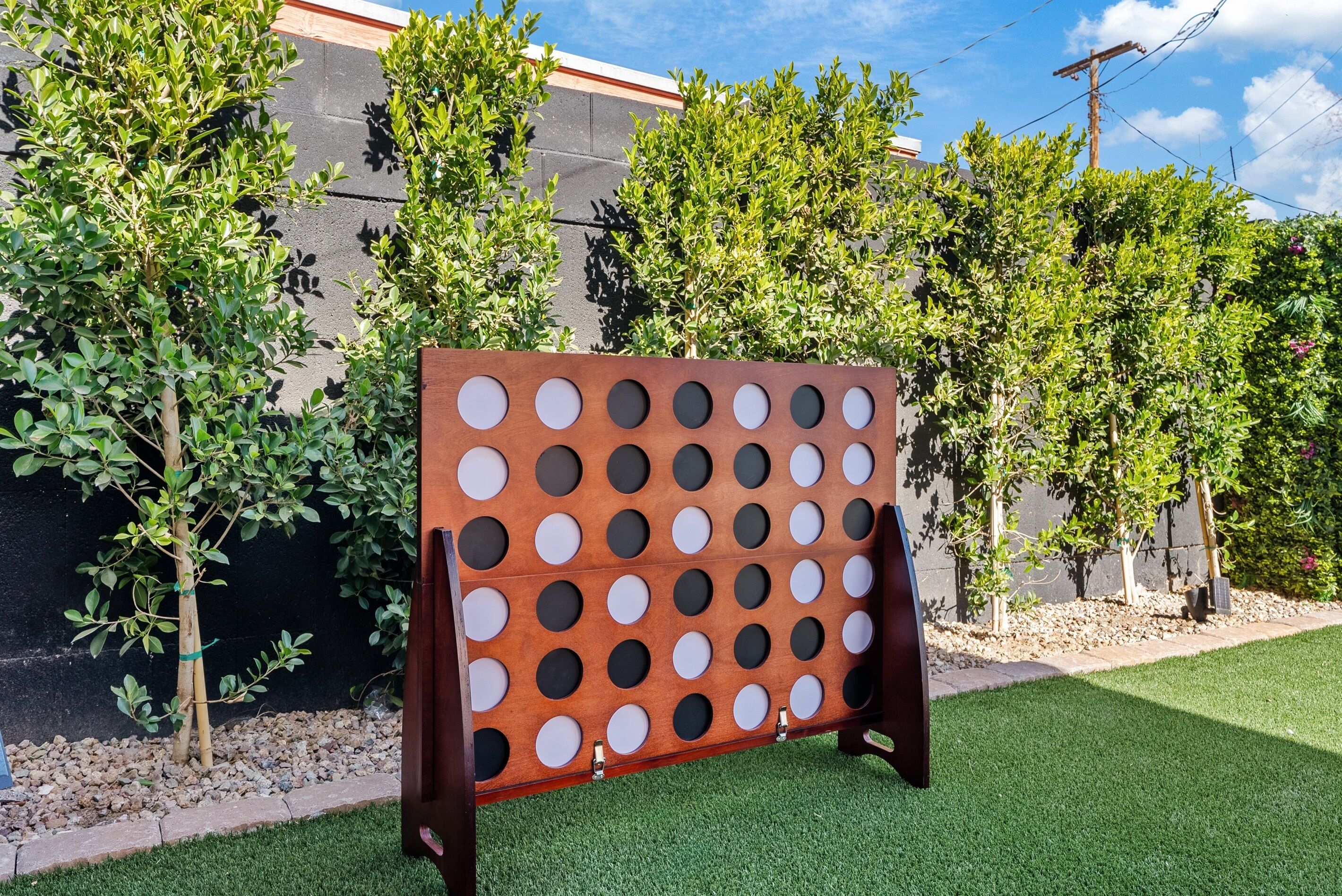 Un juego de tablero con sistema de agujeros montado al aire libre, con un edificio y árboles al fondo.