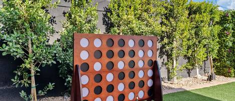 Un juego de tablero con sistema de agujeros montado al aire libre, con un edificio y árboles al fondo.