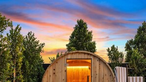 A wooden sauna with a glass door, surrounded by a garden with a lawn and trees. - Old Town | Pool | Spa | Sauna | City of Sunsets (Scottsdale)