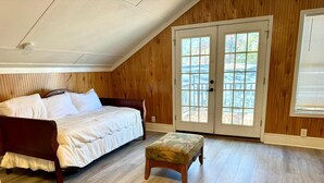 Un dormitorio con techo de paneles de madera, una cama con ropa blanca, un banco de madera y un ventanal corredizo que da a una terraza.