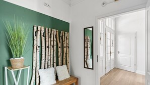 Un pasillo con pared verde, un banco de madera con cojines blancos y una planta colgante.
