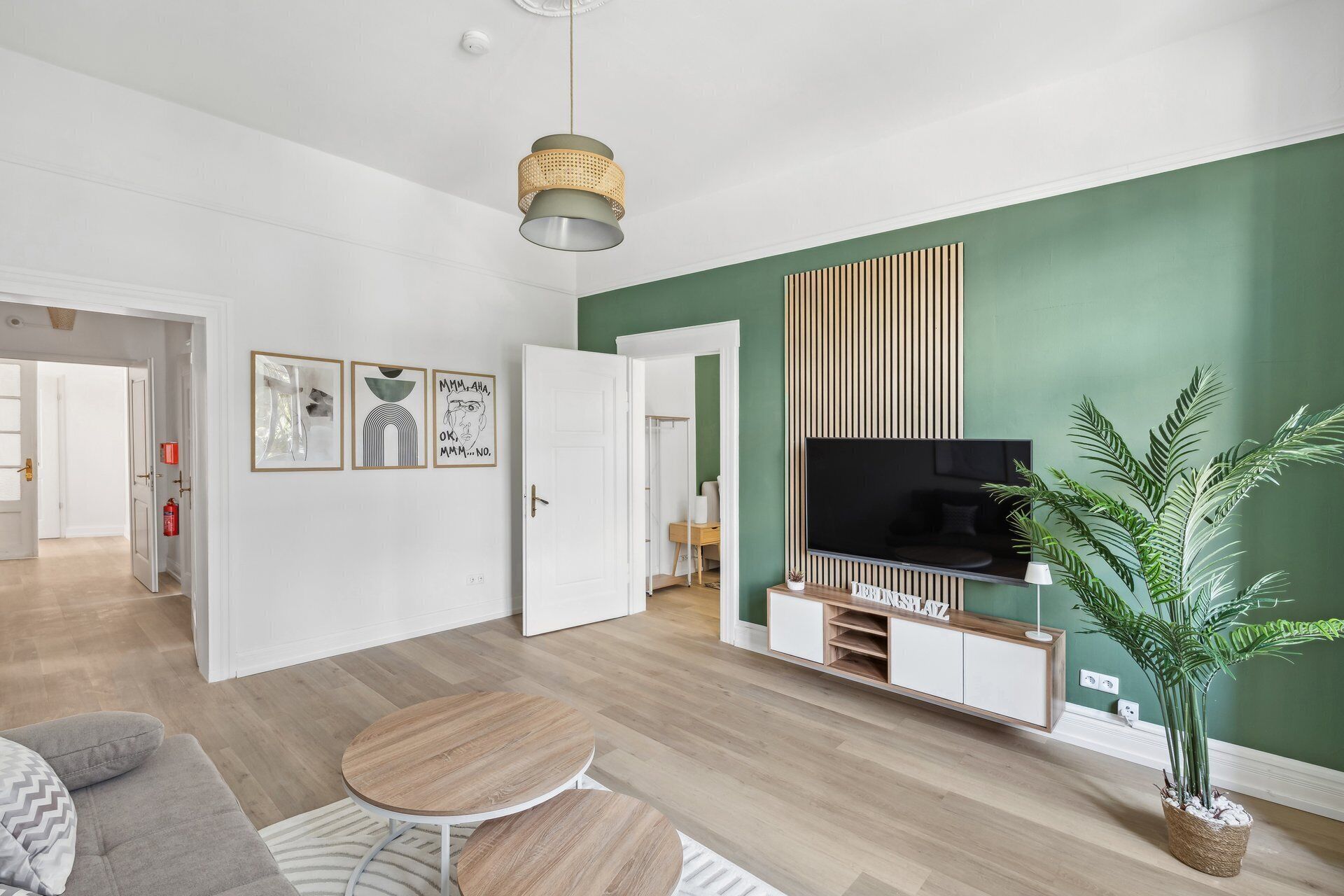 A modern living room with a flat-screen TV, a wooden coffee table, and a green accent wall.