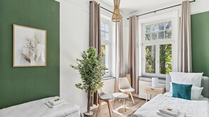 Una habitación de hotel moderna con dos camas, un ventanal grande, una planta en maceta y una pequeña mesa con sillas.