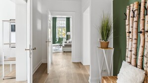 Un pasillo con suelo de madera, paredes blancas y una cortina verde al fondo.