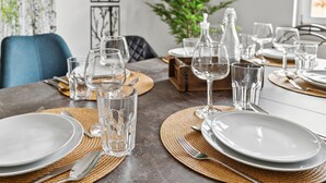 Una mesa de comedor dispuesta con cristalería transparente y platos, rodeada de individuales tejidos y una caja de madera.