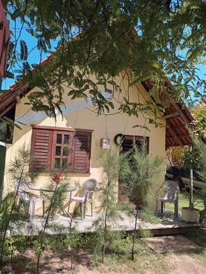 Una casa con fachada amarilla, contraventanas de madera y un porche con sillas de plástico.