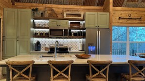 A rustic kitchen with wooden cabinets, a central island with bar stools, a stainless steel refrigerator, and a water dispenser.