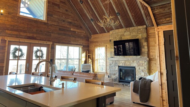 A spacious living area with a stone fireplace, wooden ceiling, and a large island with a sink.