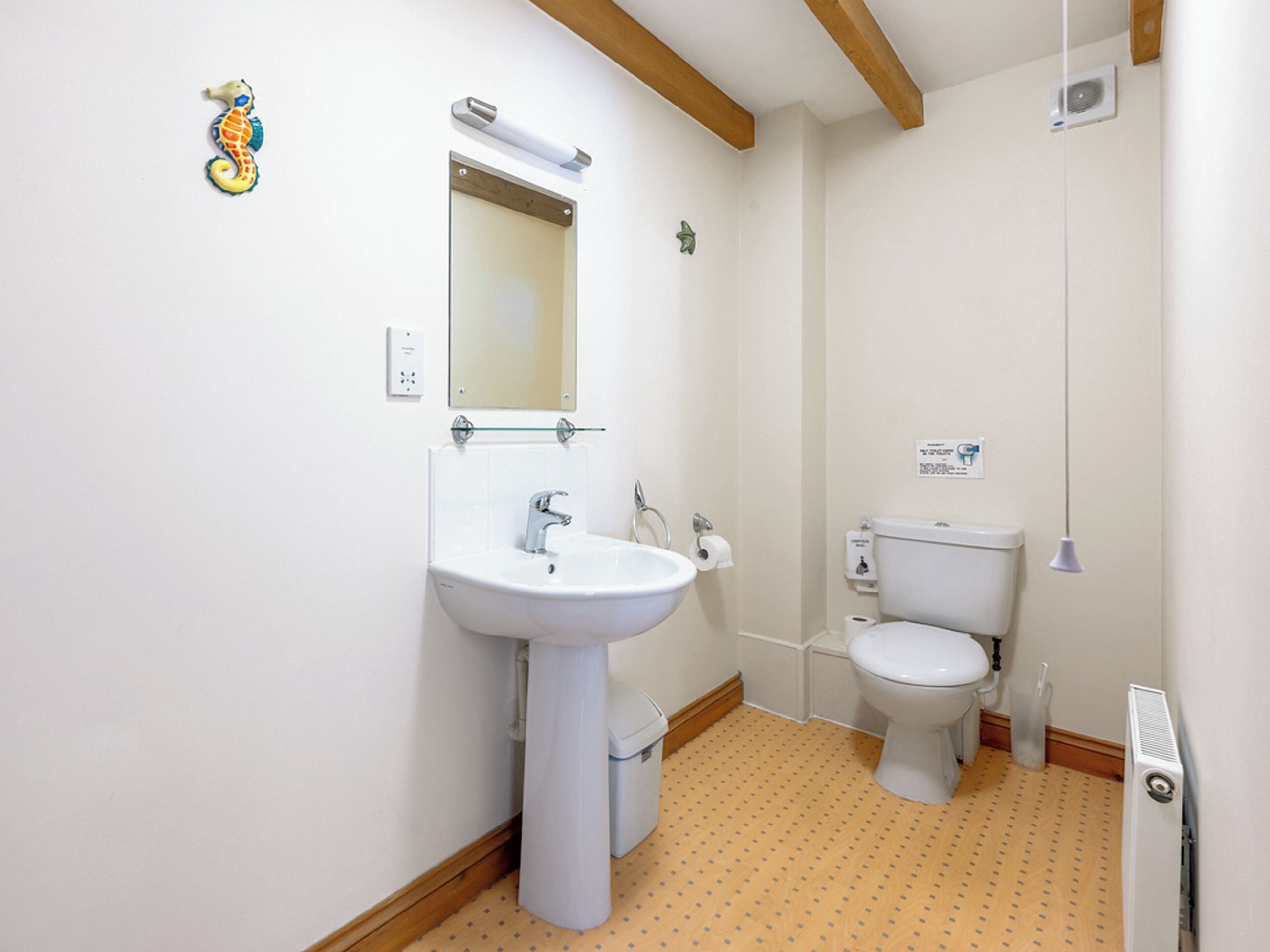 A bathroom with a white sink, mirror, and toilet. There is a wooden beam ceiling and a radiator on the wall.