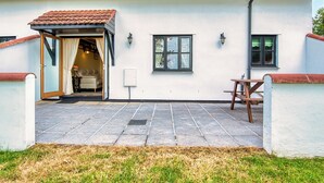 Ein zweistöckiges Gebäude mit Ziegeldach, überdachter Veranda und einer Terrasse mit Tisch und Stühlen.