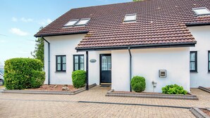 Ein zweistöckiges Haus mit Ziegeldach, einer Veranda und einem kleinen Garten.