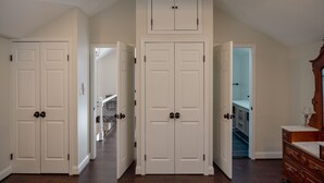 A hallway with white double doors, wooden beams on the ceiling, and a staircase in the background.