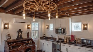 A rustic kitchen with wooden beams, white cabinets, and a vintage chandelier.