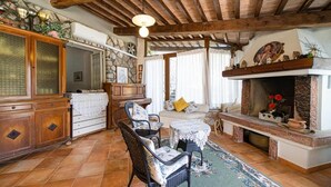 A rustic interior with a stone fireplace, wooden beams, wicker furniture, and a tiled floor. - Villa with private beach and pool (Toscana)