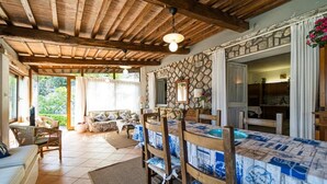 A cozy living room with a wooden ceiling, a stone wall, and a dining table with blue and white patterned tablecloths. - Villa with private beach and pool (Toscana)