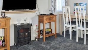 Een gezellige kamer met een televisie, een houten tafel, een stoel, een klein kastje en een houtkachel.