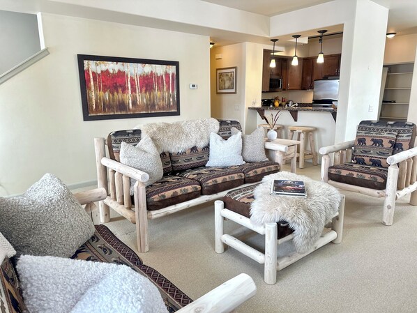 A living room with a sofa, two armchairs, and a coffee table. There is a kitchen in the background. - Modern Rustic 3 Bedroom with Pool and Hot tub (Hailey)