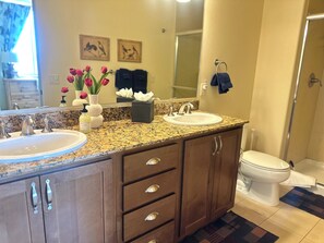 A bathroom with two sinks, a mirror, and a toilet. There are decorative items on the counter, including a vase with flowers and a soap dispenser. - Modern Rustic 3 Bedroom with Pool and Hot tub (Hailey)