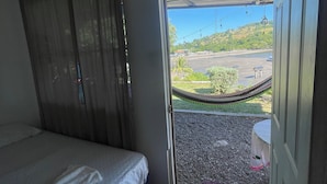 A room with a bed, a door leading outside, and a view of a beach and parking area. - Hostal Rancho Crustáceo del Pacifico (La Unión)
