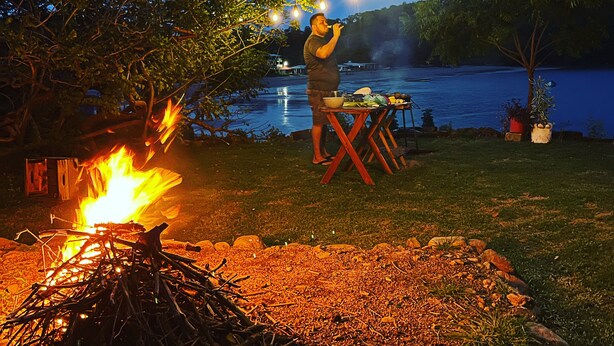 A campfire with a table and chairs set up under string lights by a lake at night. - Hostal Rancho Crustáceo del Pacifico (La Unión)