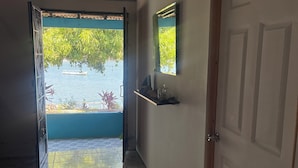 A hallway with a tiled floor, a door, a shelf with decorative items, and a view of a body of water with a boat and greenery outside. - Hostal Rancho Crustáceo del Pacifico (La Unión)