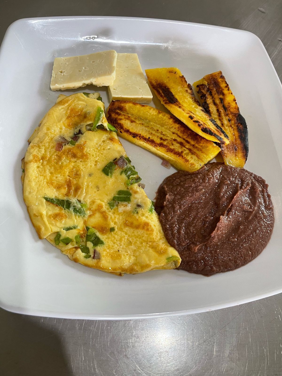 A plate with an omelette, grilled plantains, a slice of cheese, and a portion of meat.